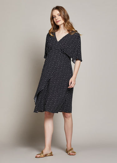 Pregnant Woman wearing a black polka dot dress against a neutral background